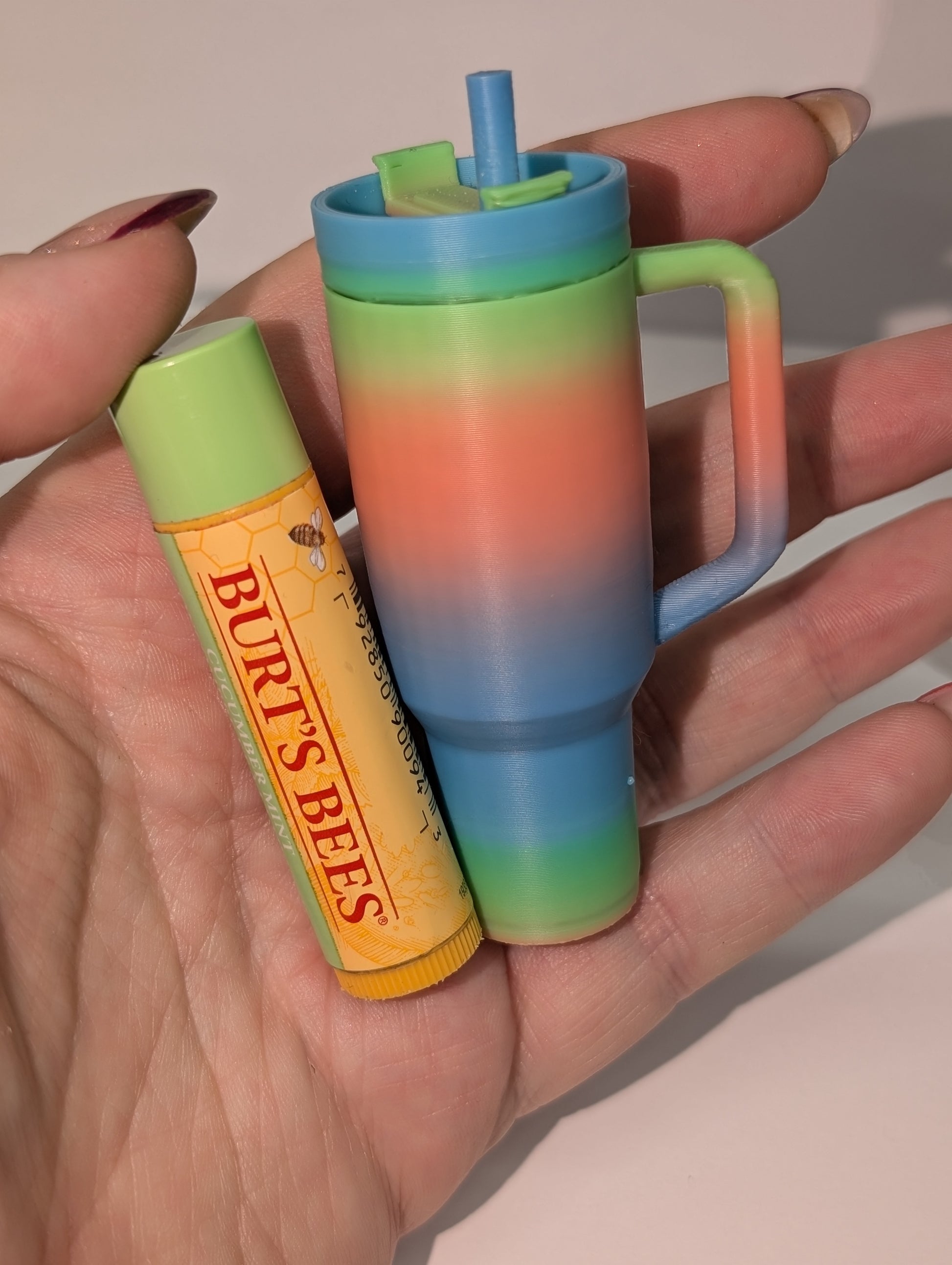 Colorful tumbler with a Burt's Bees lip balm held in a hand against a neutral background